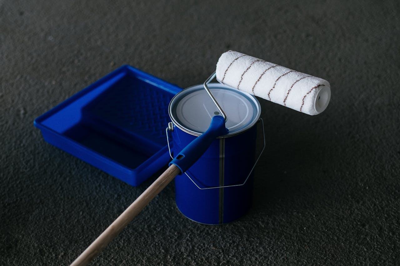 Services-01 Close-up of a paint can, roller, and tray on a textured floor, perfect for DIY projects.